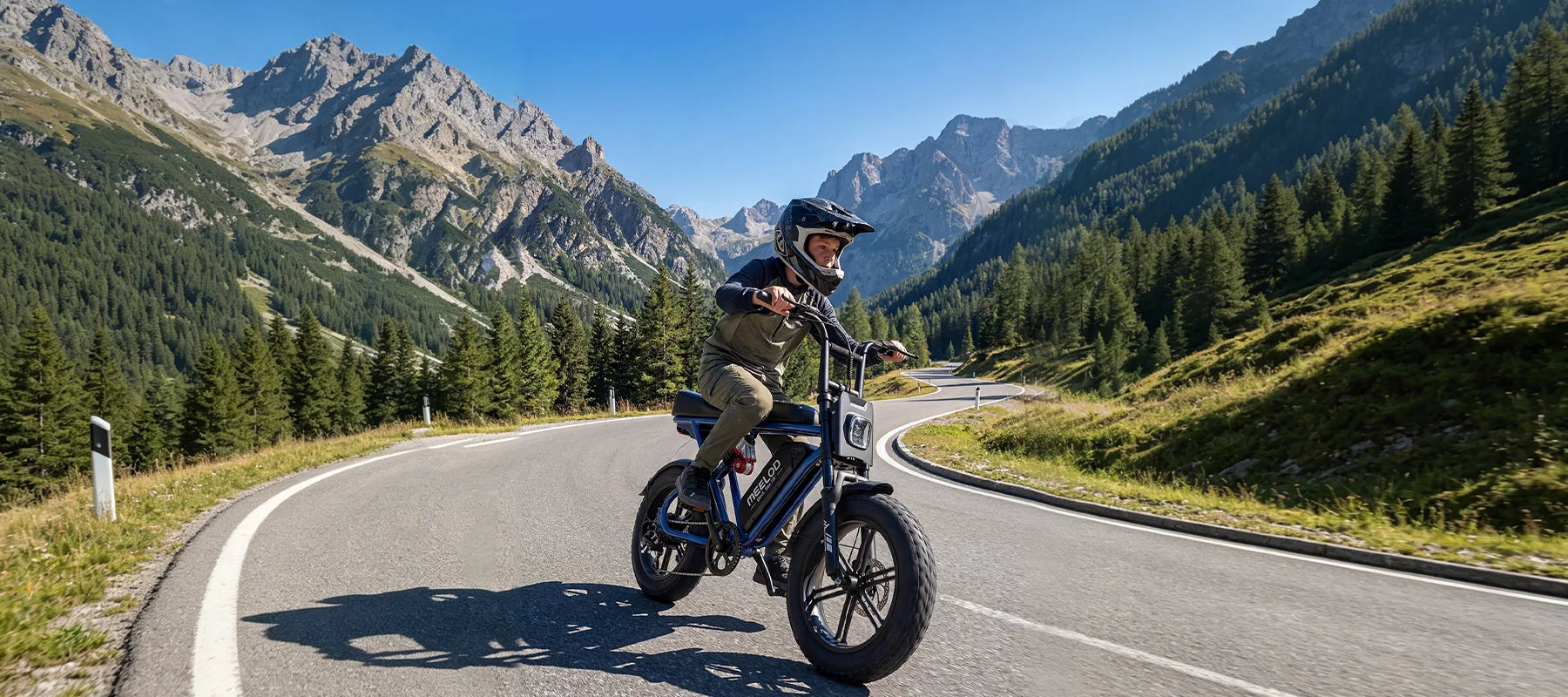 Rider on MEELOD moped style fat tire ebike cruising mountain road with alpine scenery – retro electric bike built for adventure